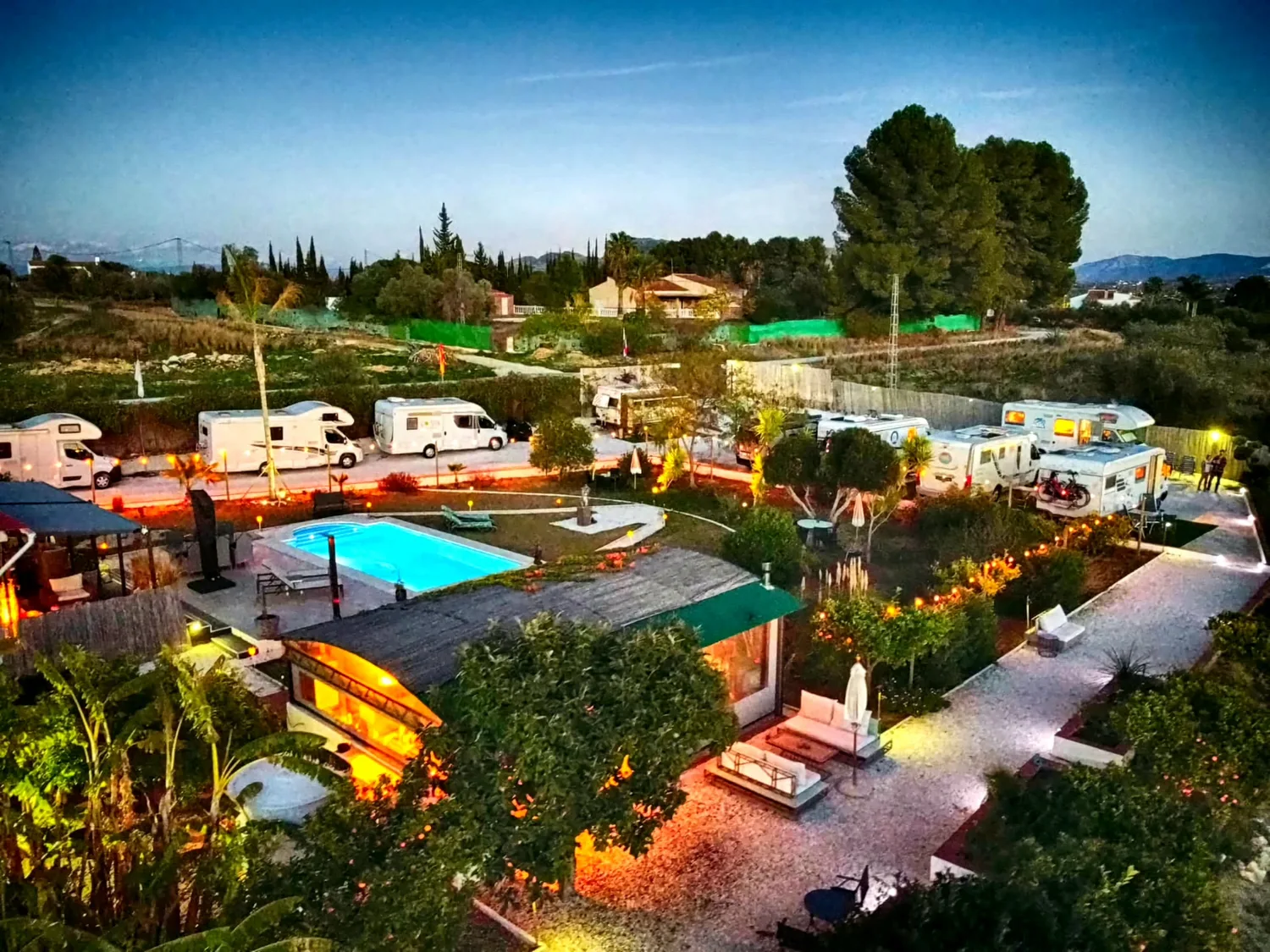 Het Go Spain terrein in de schemering: verlicht zwembad, campers en tuin